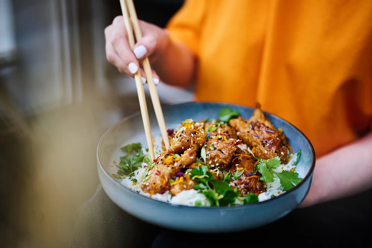 Glazed sesame-topped pieces over rice in a blue bowl with chopsticks, similar to this salmon bowl recipe