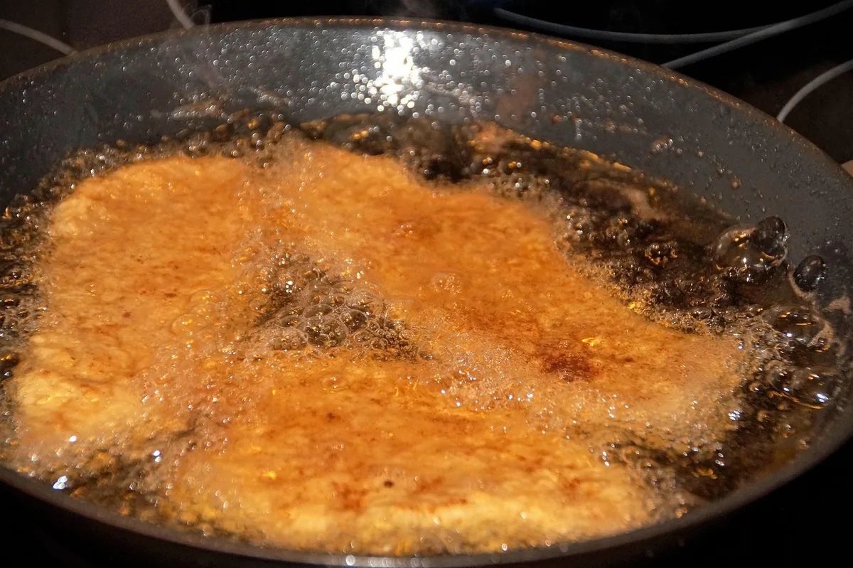 Breaded cutlets pan-frying in hot oil in a dark skillet until golden