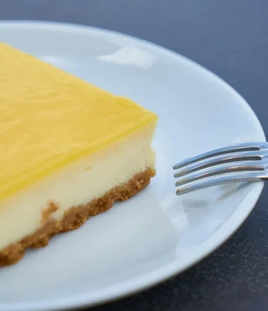 Square of lemon-topped cream cheese dessert on a white plate with a fork, similar to a lemon cream cheese dump cake
