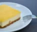 Square of lemon-topped cream cheese dessert on a white plate with a fork, similar to a lemon cream cheese dump cake