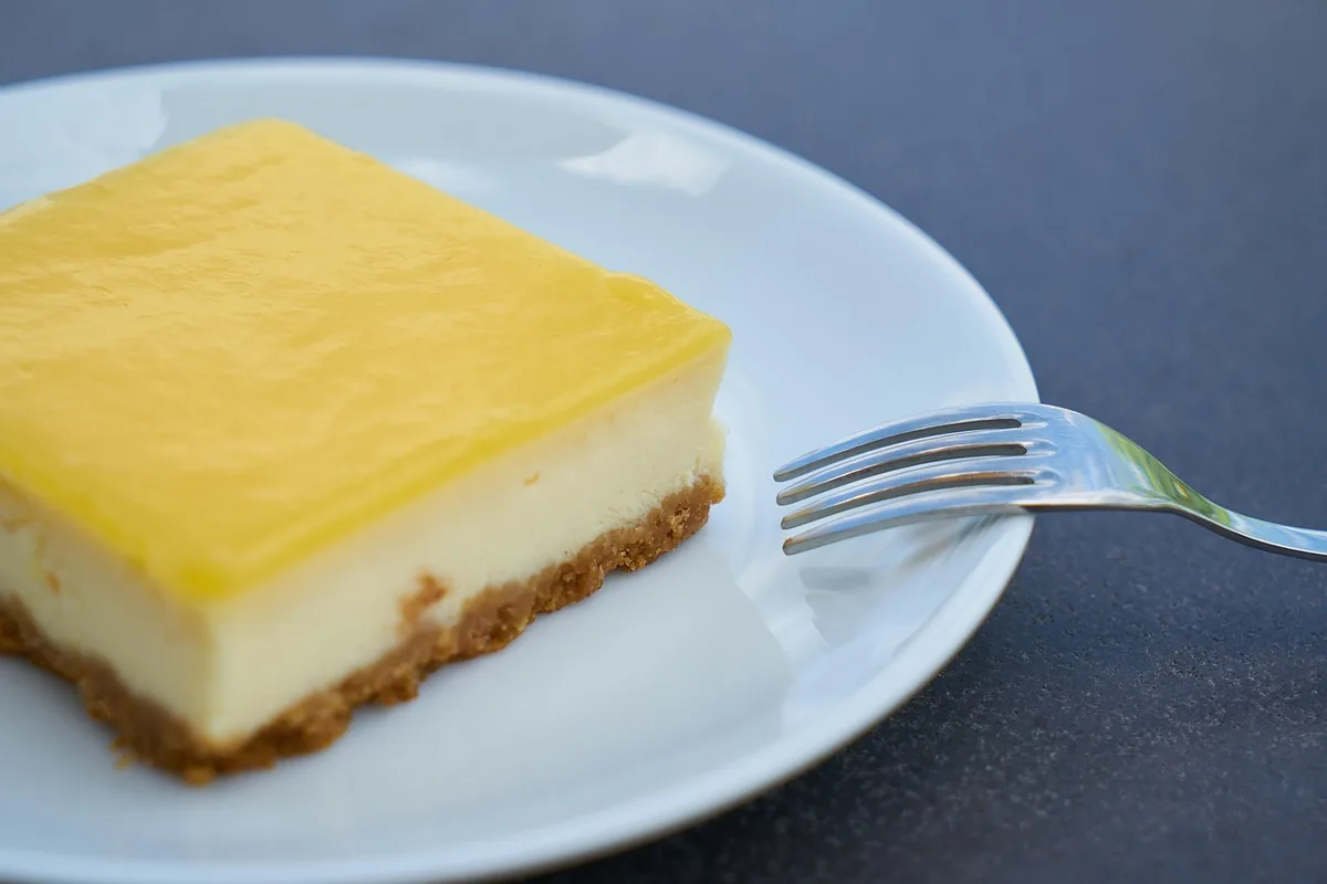 Square of lemon-topped cream cheese dessert on a white plate with a fork, similar to a lemon cream cheese dump cake