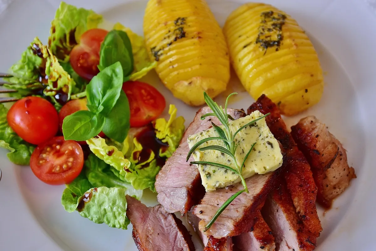 Sliced seared steak topped with herb butter and rosemary, served with hasselback potatoes and salad
