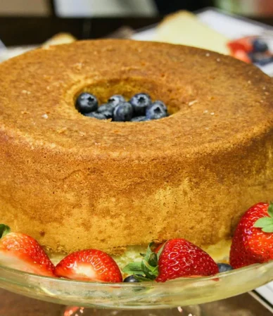 Golden tube pound cake on a glass stand surrounded by fresh strawberries, similar to this strawberry pound cake