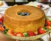 Golden tube pound cake on a glass stand surrounded by fresh strawberries, similar to this strawberry pound cake