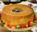 Golden tube pound cake on a glass stand surrounded by fresh strawberries, similar to this strawberry pound cake