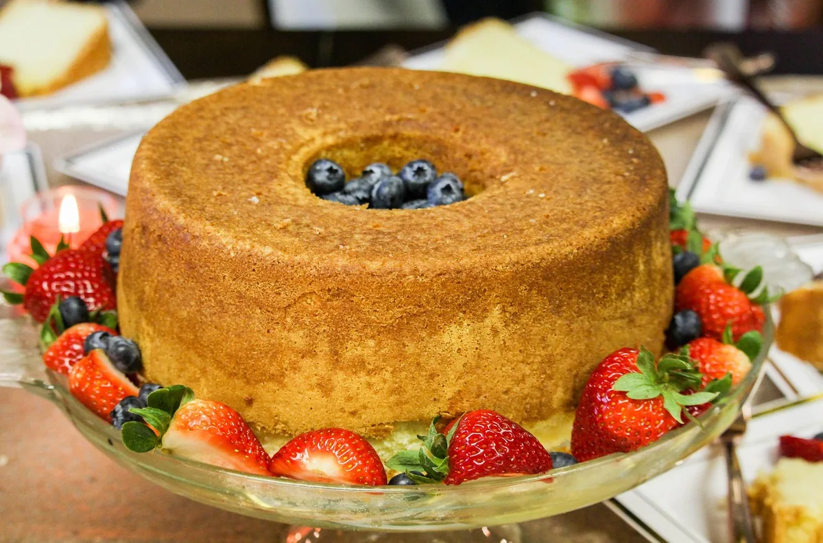 Golden tube pound cake on a glass stand surrounded by fresh strawberries, similar to this strawberry pound cake