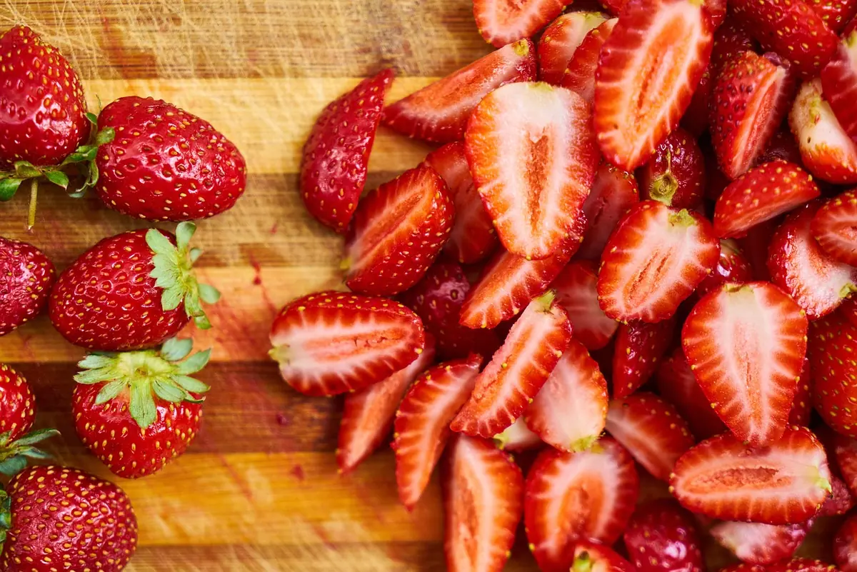 Fresh strawberries halved and sliced on a wooden cutting board, ready to dice for the cake batter