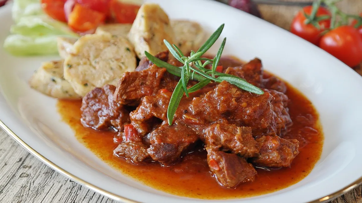 Tender braised beef in tomato sauce served on a white plate with dumplings