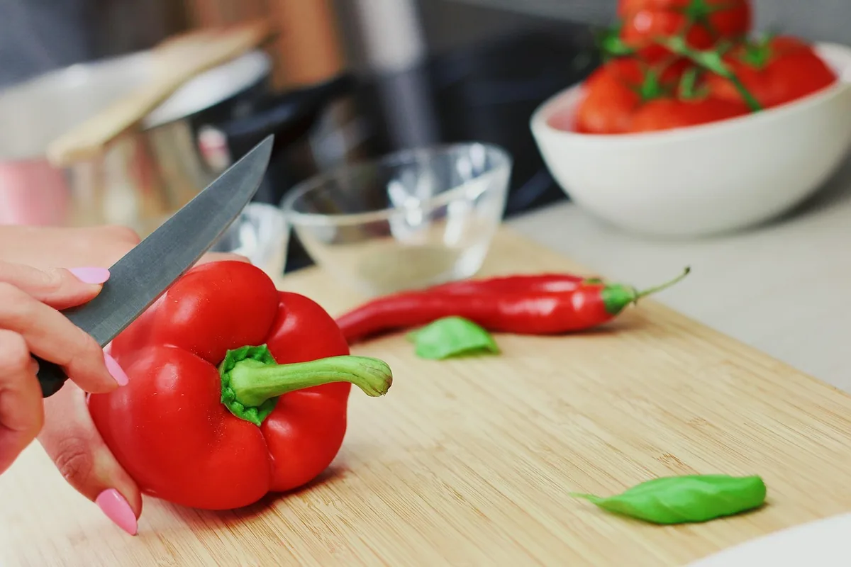 Slicing a green-stemmed red bell pepper on a cutting board for the tomato braising sauce