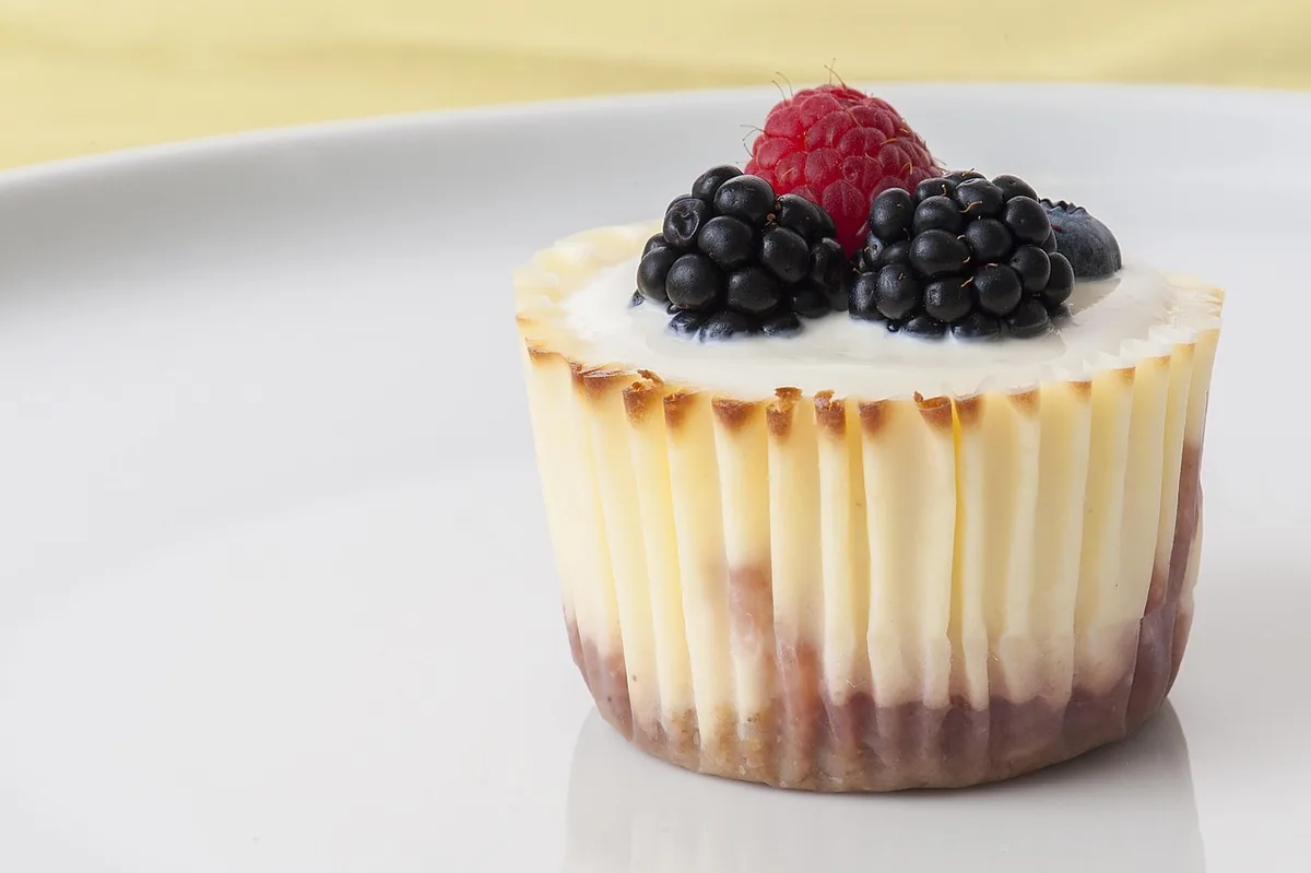 A mini cheesecake in a paper liner topped with blackberries and a raspberry, similar to this mini cheesecake recipe