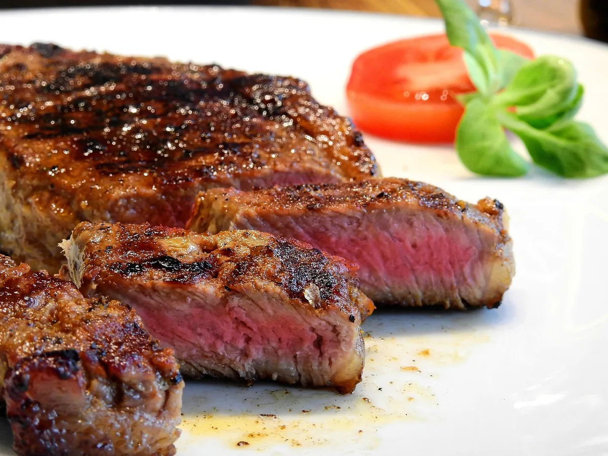 Seared steak sliced across the grain on a white plate with tomato and greens