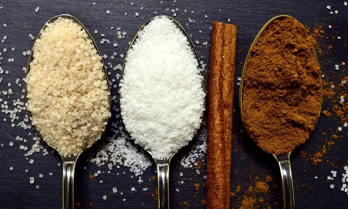 Spoons of brown sugar, white sugar and ground cinnamon with a cinnamon stick for a cinnamon sugar swirl filling