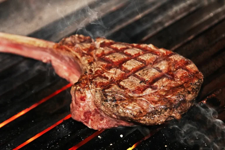 Thick tomahawk steak with crosshatch grill marks on hot grates, similar to the ribeye in this how to grill steak guide