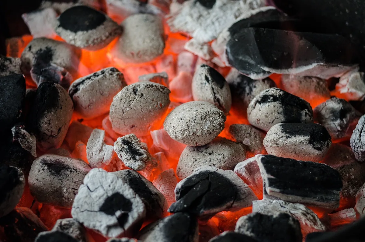 Glowing charcoal briquettes covered in gray ash, ready for a two-zone fire to grill steak