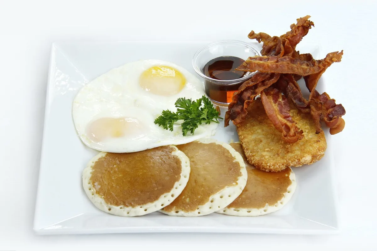 Diner-style breakfast plate with fried eggs, crisp bacon, a hash brown patty and small pancakes