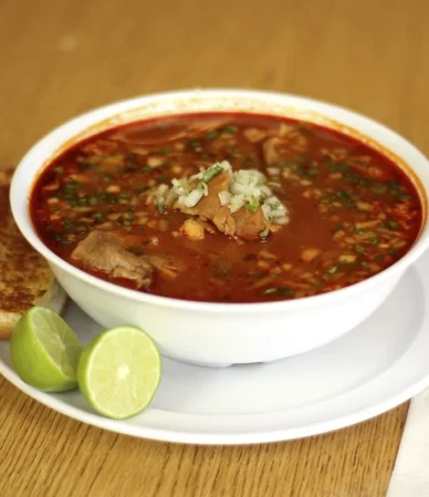 Bowl of red chile soup with lime wedges, similar to a creamy chicken enchilada soup