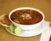 Bowl of red chile soup with lime wedges, similar to a creamy chicken enchilada soup