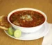 Bowl of red chile soup with lime wedges, similar to a creamy chicken enchilada soup