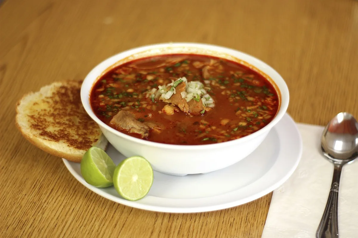 Bowl of red chile soup with lime wedges, similar to a creamy chicken enchilada soup