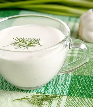 Glass cup of creamy white sauce topped with a dill sprig, similar to a lemon dill sauce for salmon