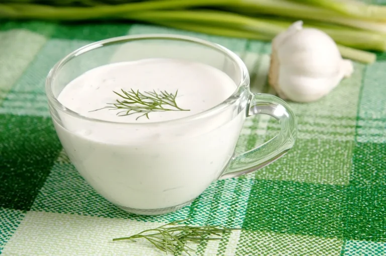 Glass cup of creamy white sauce topped with a dill sprig, similar to a lemon dill sauce for salmon