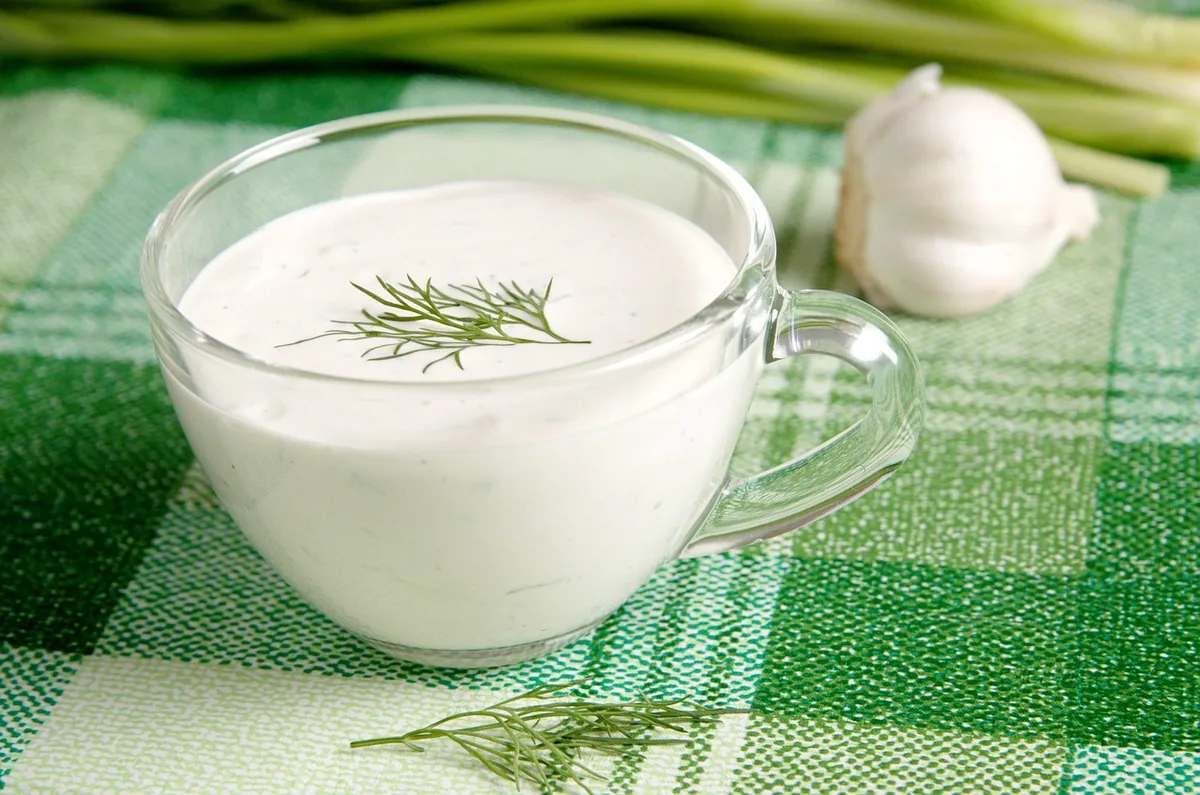 Glass cup of creamy white sauce topped with a dill sprig, similar to a lemon dill sauce for salmon
