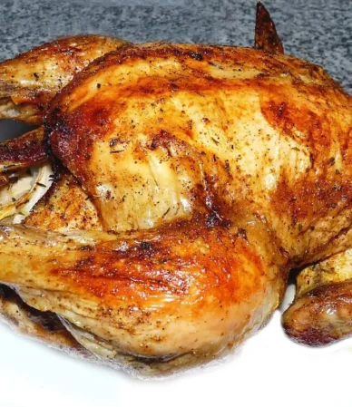 Golden roasted whole chicken with crisp, seasoned skin on a white plate, similar to beer can chicken