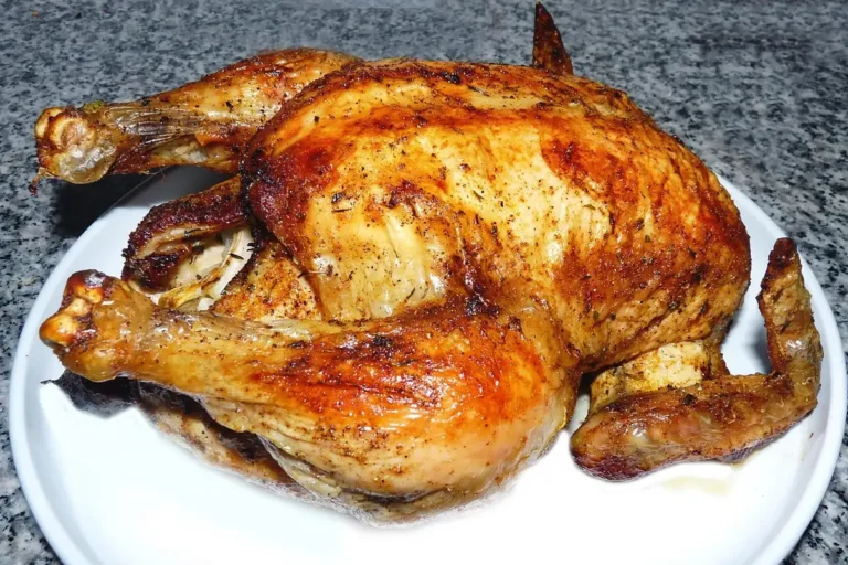 Golden roasted whole chicken with crisp, seasoned skin on a white plate, similar to beer can chicken