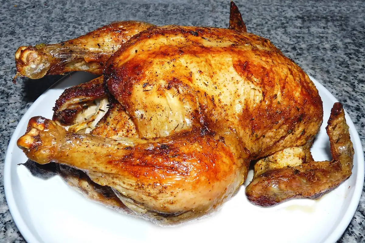 Golden roasted whole chicken with crisp, seasoned skin on a white plate, similar to beer can chicken