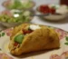 Crispy fried-shell taco filled with seasoned beef, tomato, avocado, cheese and sour cream on a floral plate, similar to ground beef tacos