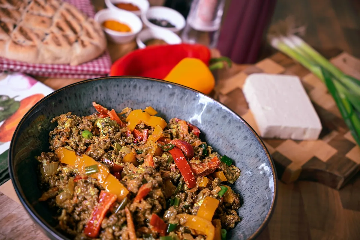 Seasoned browned ground beef with red and yellow bell peppers in a dark bowl, similar to taco meat