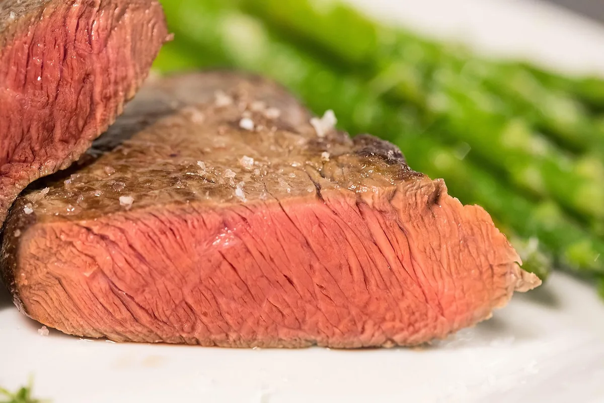 Thick steak cut open to show even pink from edge to edge with a browned crust and flaky salt, similar to how to reverse sear a steak
