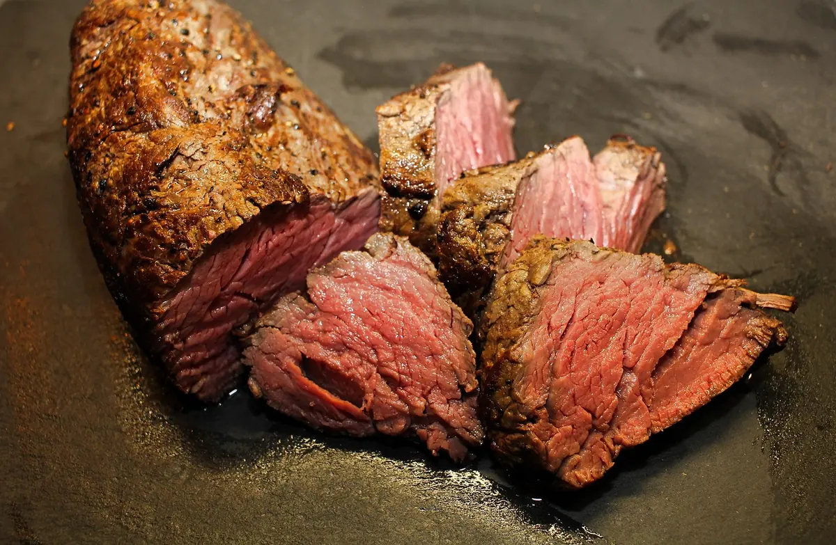 Sliced medium-rare beef steak with a dark seared crust on a black plate, similar to a reverse seared steak