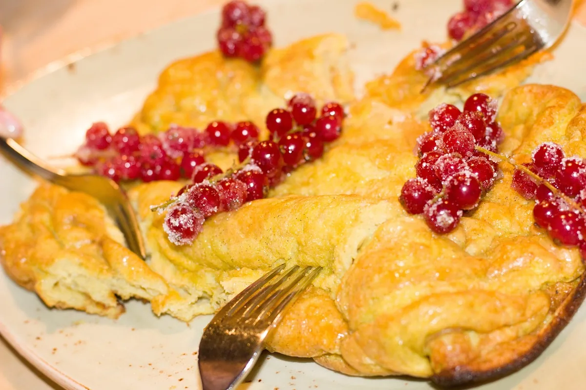 Golden puffed oven pancake topped with red currants and powdered sugar, similar to a German pancake served with berries