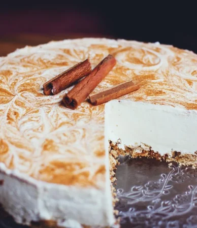 Sliced cheesecake with a golden cinnamon swirl top and cinnamon sticks, similar to churro cheesecake