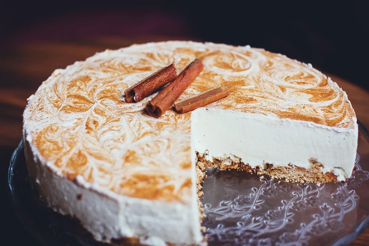 Sliced cheesecake with a golden cinnamon swirl top and cinnamon sticks, similar to churro cheesecake