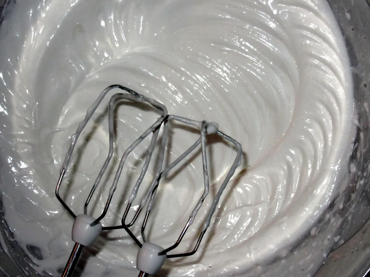 Electric mixer beaters in a smooth white mixture, the stage where the cheesecake filling turns creamy