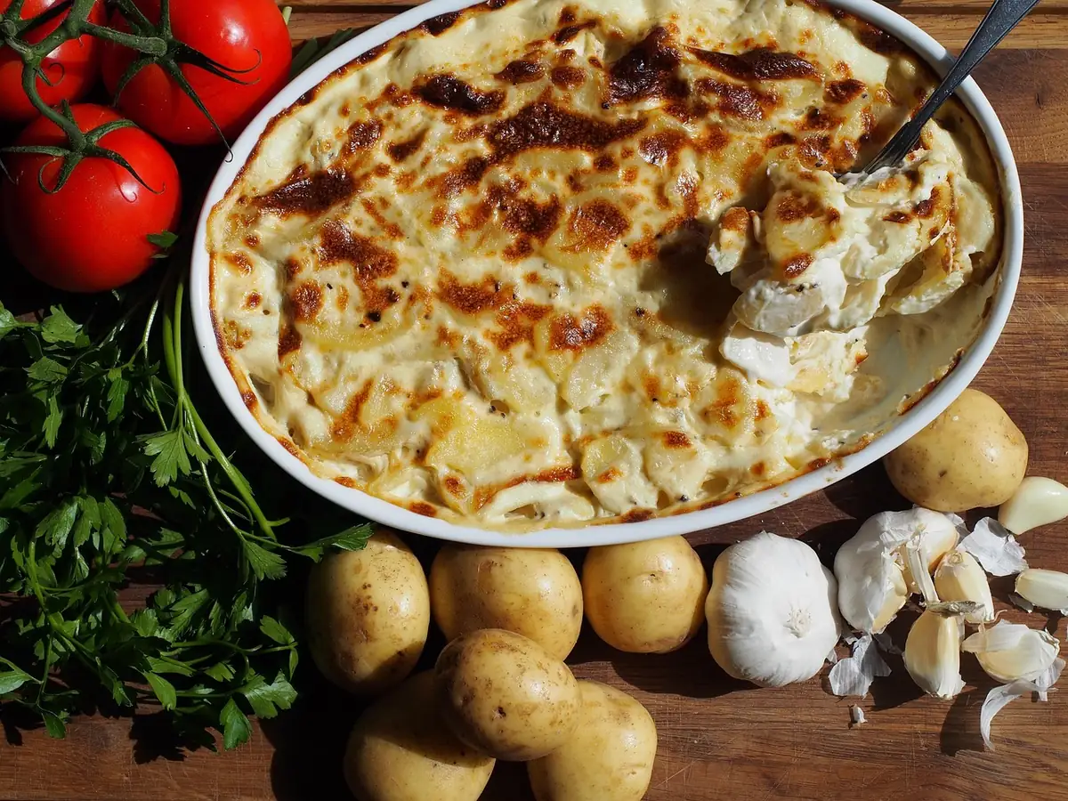 Serving spoon scooping a creamy, browned potato casserole from an oval baking dish