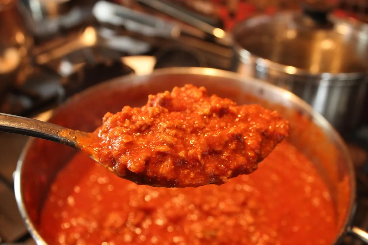 Spoonful of cooked ground beef in tomato sauce lifted from a pan, the kind of filling used in a beef noodle bake