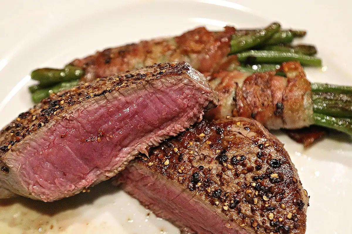 Peppercorn-crusted beef filet mignon cut in half to show a pink medium-rare center, served with green beans