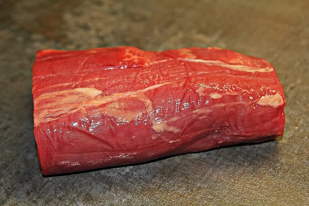 Raw center-cut piece of beef tenderloin on a slate surface, ready to be trimmed and cut into steaks
