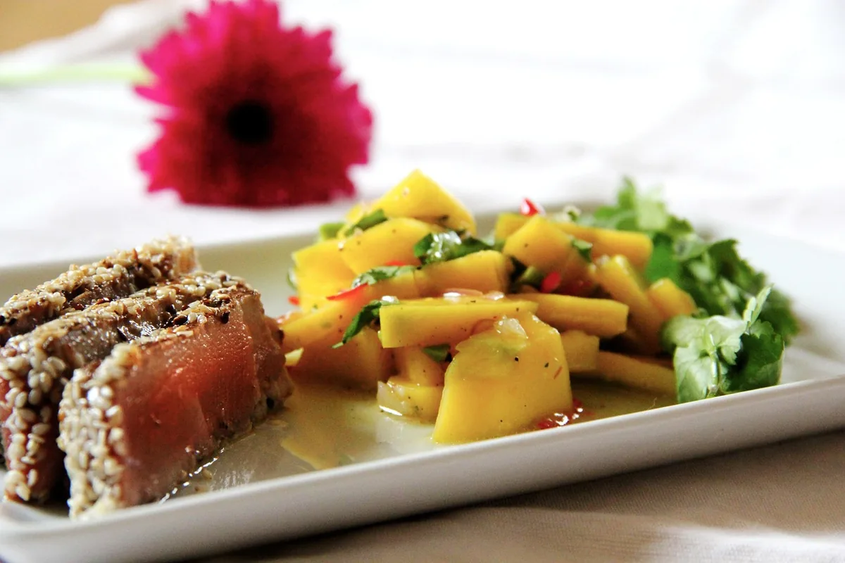 Sesame-crusted seared tuna sliced to show a rare red center, served with mango salad, similar to this tuna steak recipe