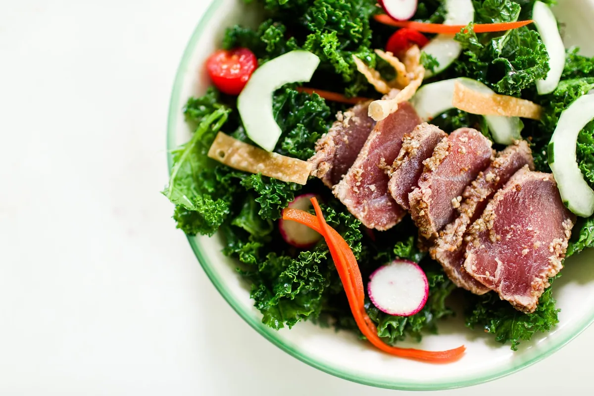 Slices of sesame-crusted seared tuna on a kale salad with cucumber, radish, carrot and crispy wonton strips