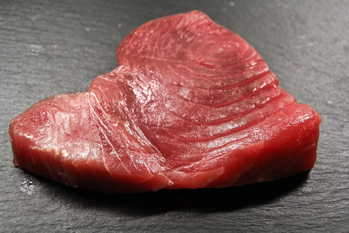 Raw ahi tuna steak with deep red flesh on a dark slate board, ready for the soy-ginger marinade