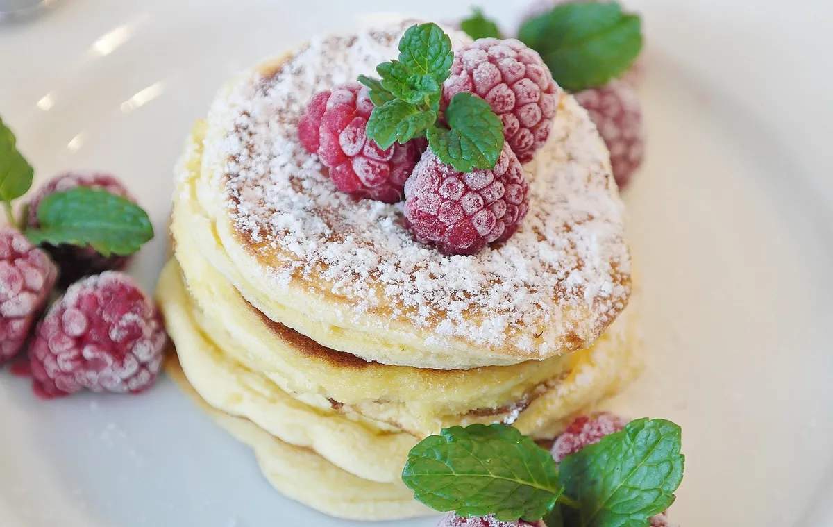 Stack of thick fluffy pancakes topped with raspberries, mint and powdered sugar, similar to souffle pancakes served with berries