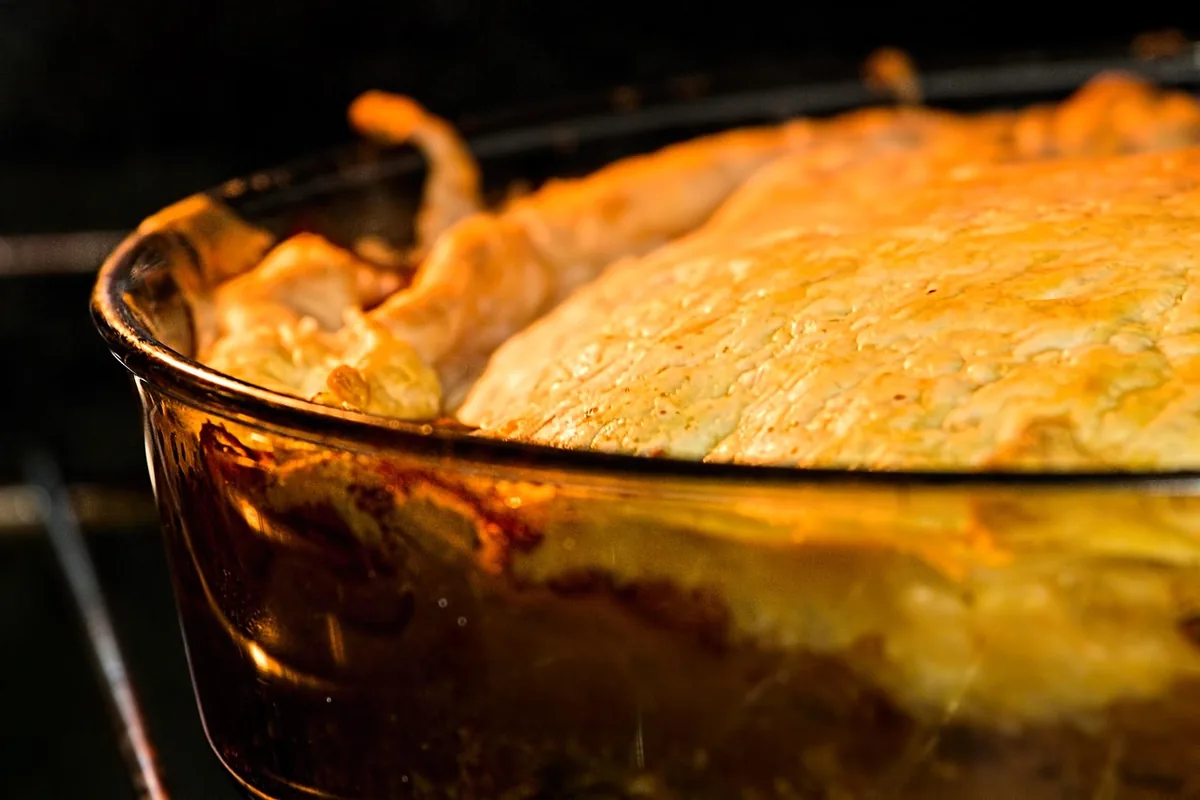 Golden baked crust bubbling in a glass baking dish in the oven, similar to this chicken cobbler recipe