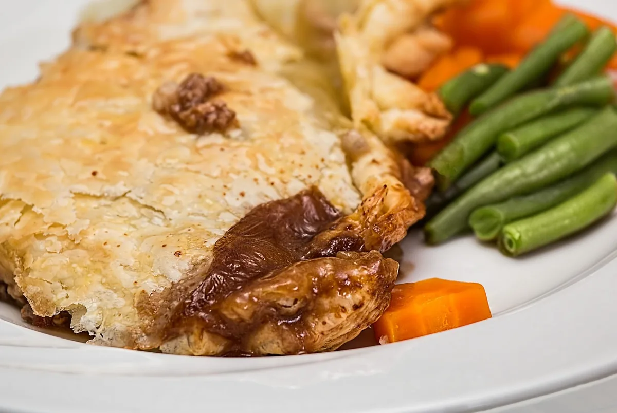 A serving of savory pie with golden crust and creamy filling, plated with green beans and carrots