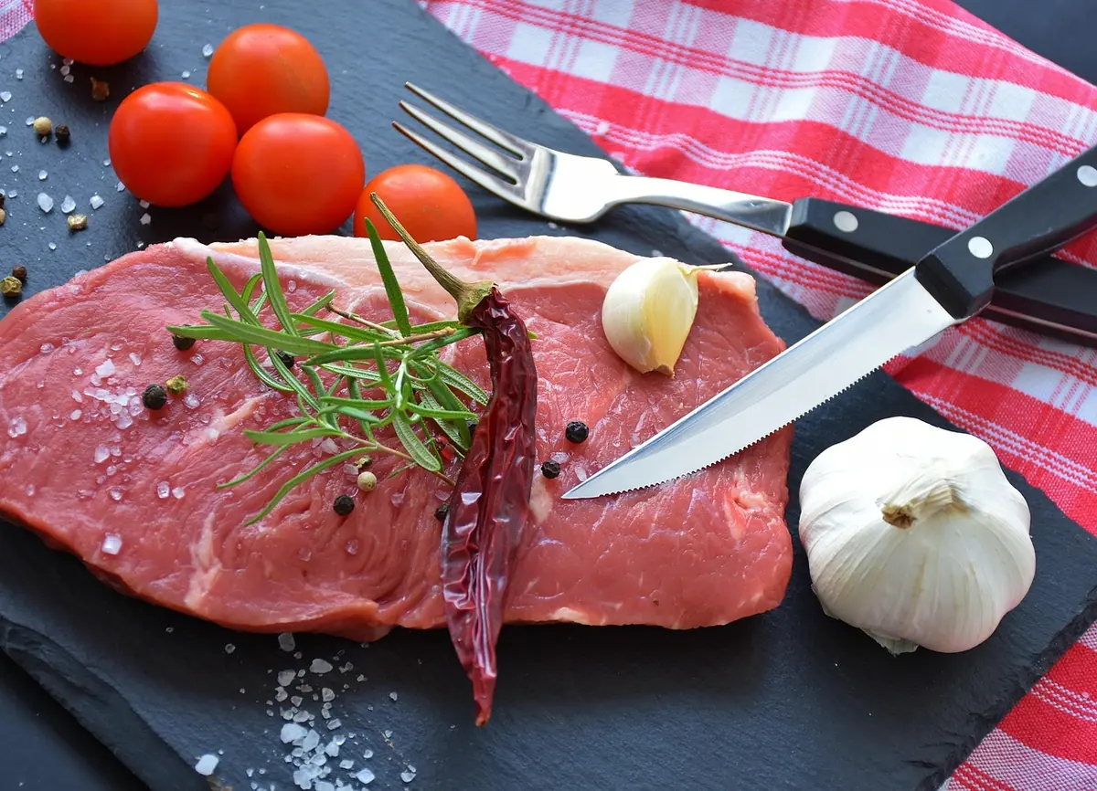 Raw lean beef steak on a slate board with rosemary, garlic and a dried chili, ready to be pounded and marinated