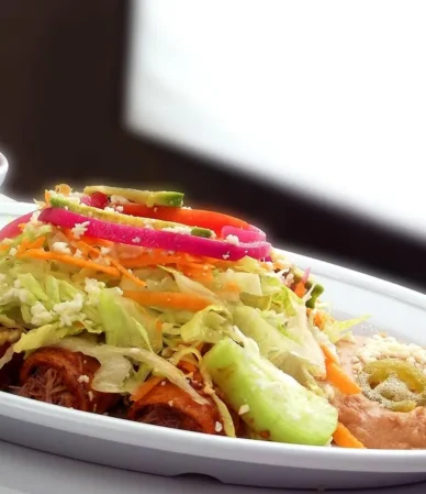 Enchiladas in red sauce topped with lettuce, onion and lime on a white platter, similar to these ground beef enchiladas