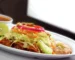 Enchiladas in red sauce topped with lettuce, onion and lime on a white platter, similar to these ground beef enchiladas